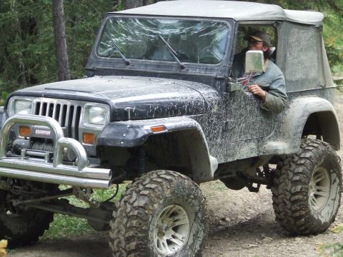 1990 Ford Bronco - A mud-splattered Jeep Wrangler navigates a wooded trail, equipped with a winch and aggressive off-road tires.