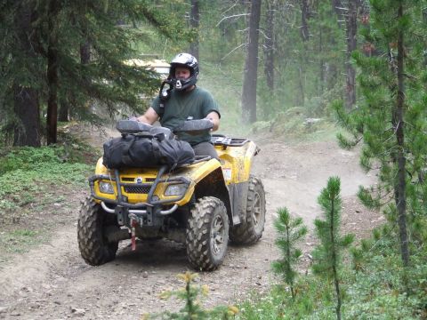 1990 Ford Bronco - A man rides a yellow ATV through a wooded area on a dusty trail.