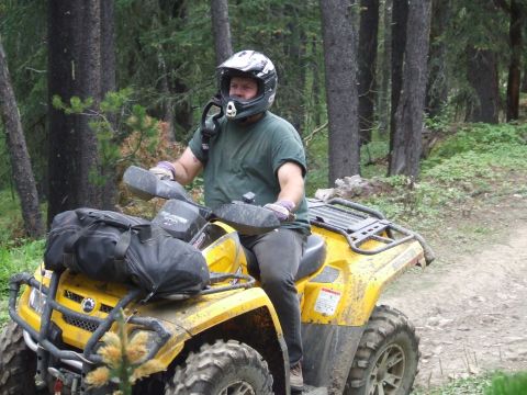 1990 Ford Bronco - A rider wearing a helmet and green shirt navigates a muddy trail on a yellow ATV.