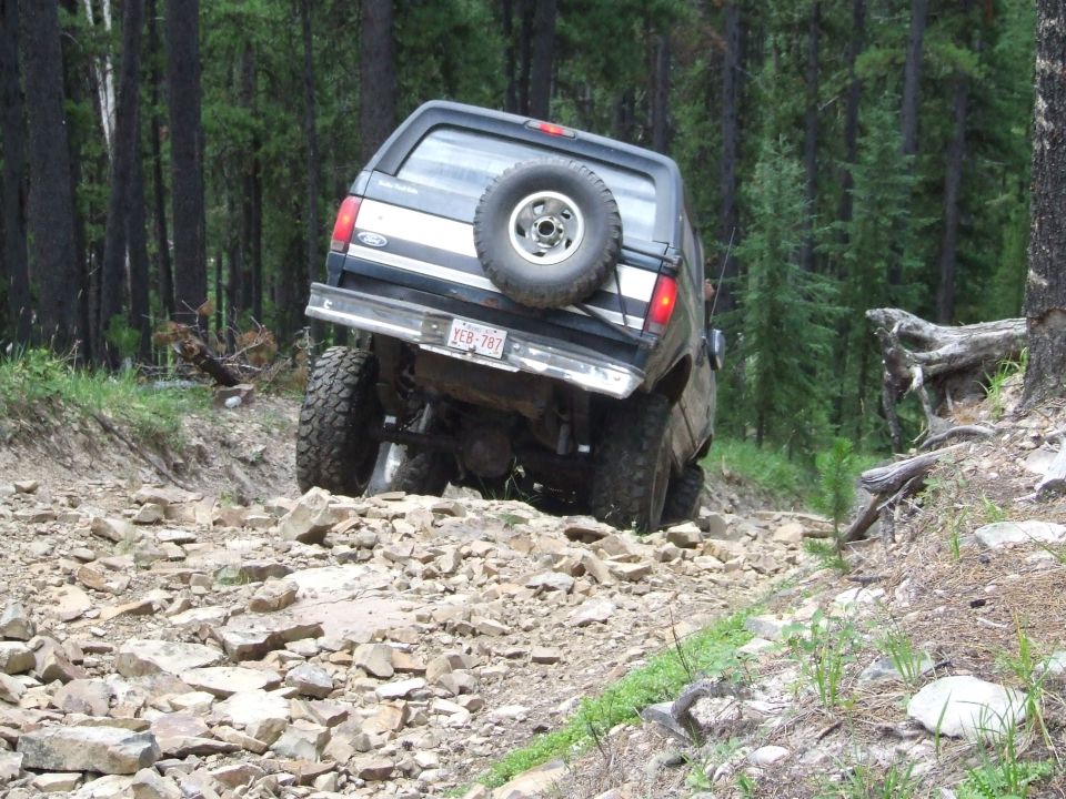 1990 Ford Bronco climbing a steep, rocky forest trail, rear view