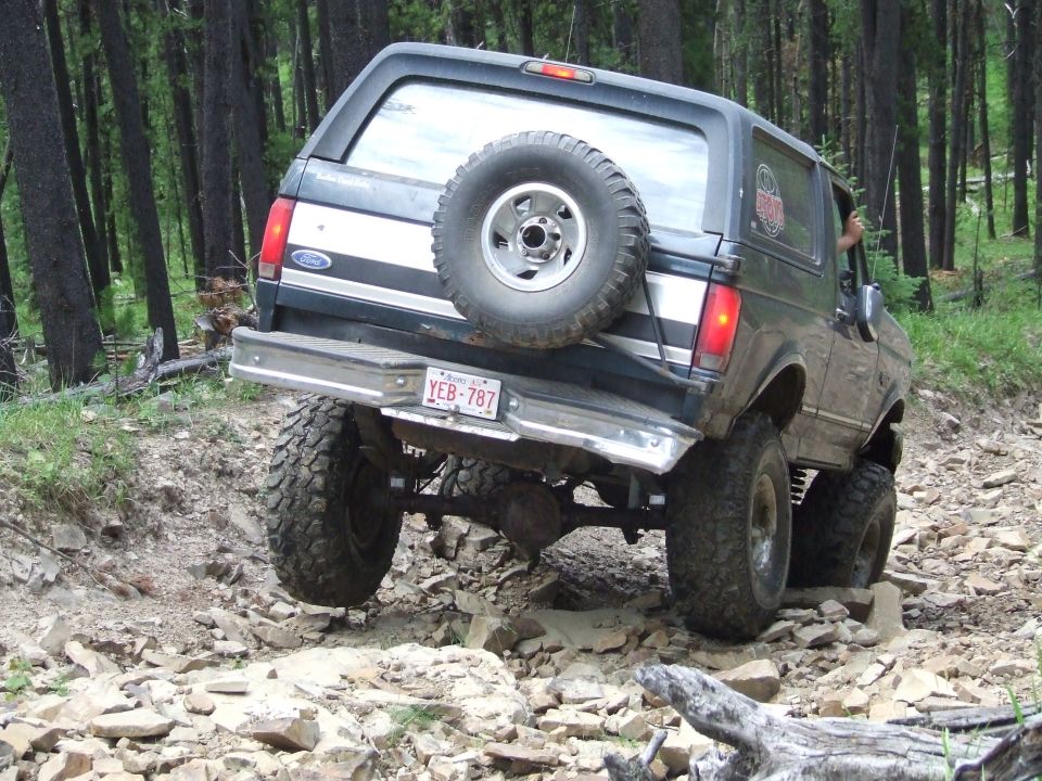 Ford Bronco climbing over rocks on a wooded trail
