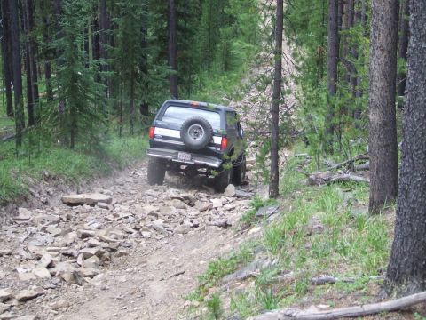 1990 Ford Bronco - Ford Bronco navigates a challenging, rocky path through a dense forest.