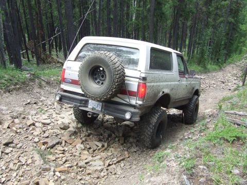 1990 Ford Bronco - A white Ford Bronco navigates a rocky, wooded trail.