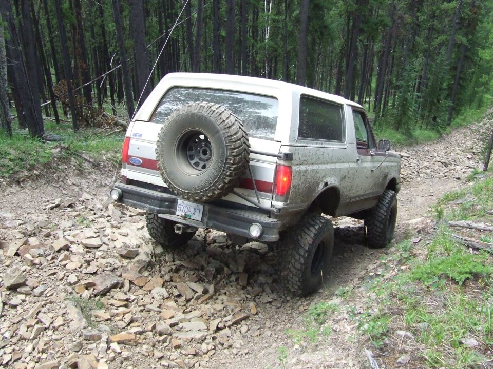 White Ford Bronco with spare tire on rear, driving on rocky trail