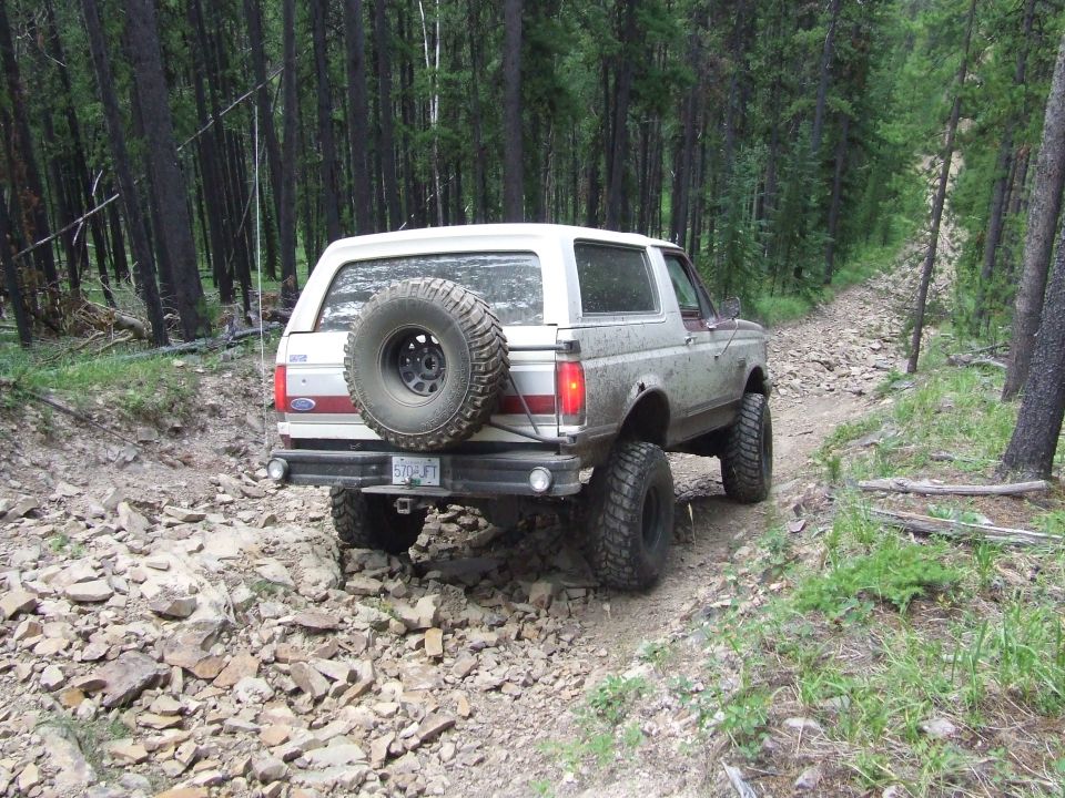 White 1990 Ford Bronco on a rocky forest trail, rear view