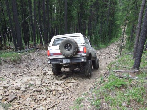 1990 Ford Bronco - Ford Bronco navigates a challenging, rocky path through a dense forest.