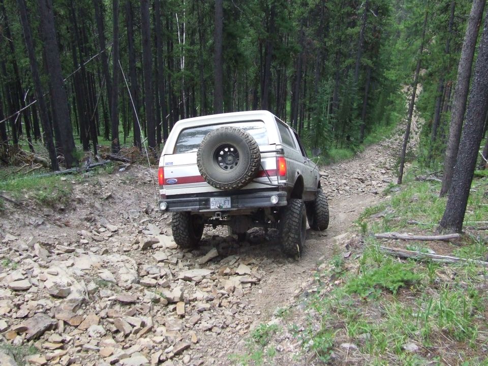 1990 Ford Bronco driving on a rocky, wooded trail