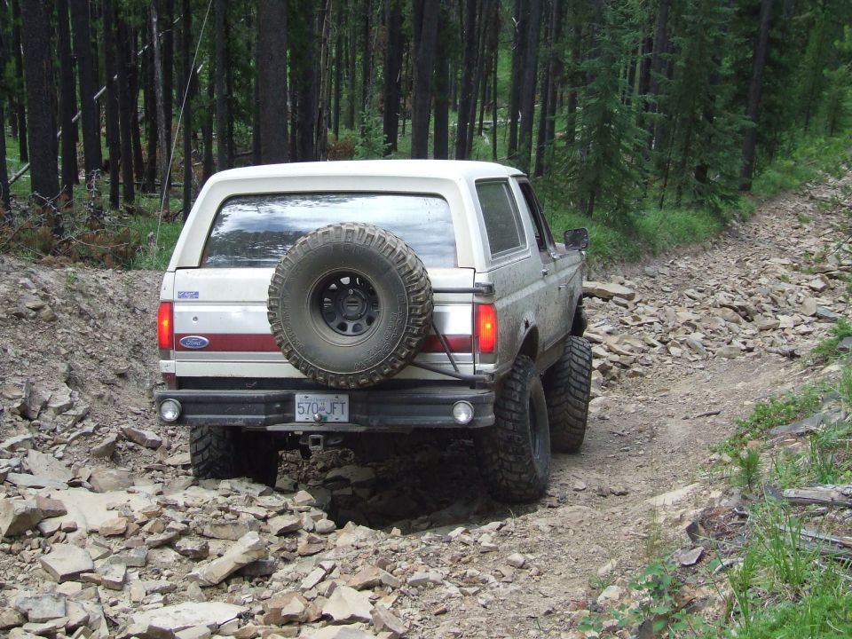 White Ford Bronco with a spare tire on the back, driving on a rocky dirt road