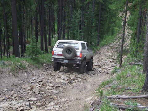 1990 Ford Bronco - Ford Bronco navigates a challenging rocky path through a dense forest.
