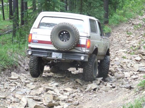 1990 Ford Bronco - A Ford Bronco navigates a challenging, rocky off-road path through a wooded area.