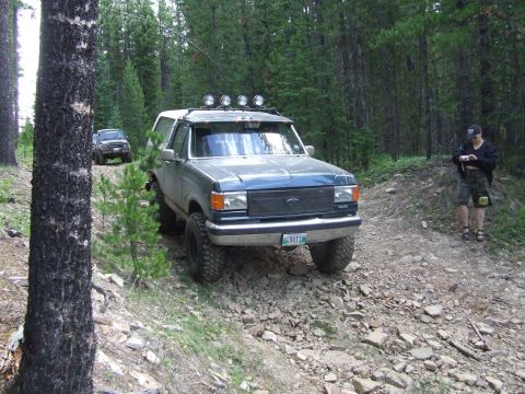 1990 Ford Bronco - Two SUVs navigate a wooded trail during an off-road event.