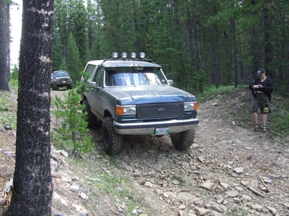 1990 Ford Bronco on a rocky dirt road in a forest, another SUV behind it