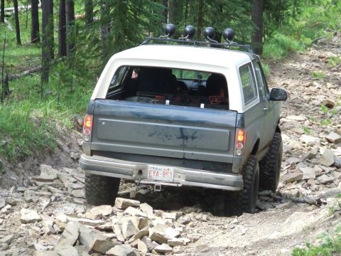 1990 Ford Bronco - A Ford Bronco navigates a challenging, rocky off-road path in a wooded area.