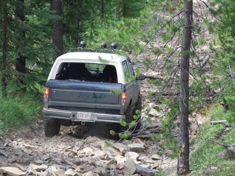 1990 Ford Bronco - A Ford Bronco navigates a challenging, rocky path through a dense forest.