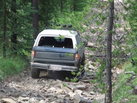 1990 Ford Bronco - A Ford Bronco navigates a challenging, rocky path through a forest.