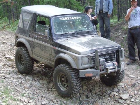 1990 Ford Bronco - A modified Suzuki Samurai navigates a rough, rocky terrain with people standing nearby.