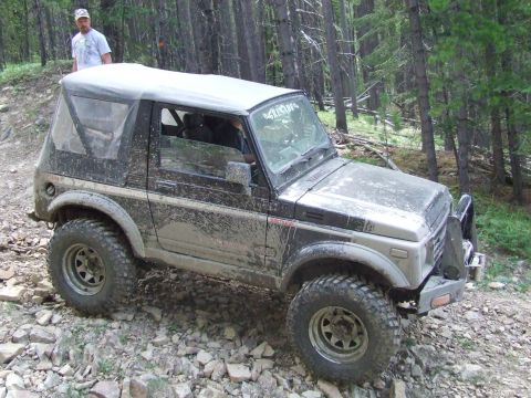 1990 Ford Bronco - A Suzuki Samurai navigates a wooded, rocky terrain during an off-road event.