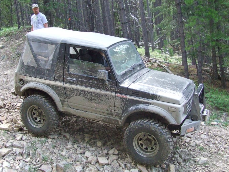Mud-splattered Suzuki Samurai with a soft top on a rocky trail