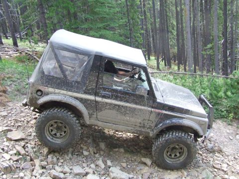 1990 Ford Bronco - Suzuki Samurai navigates a challenging rocky path through a forest.