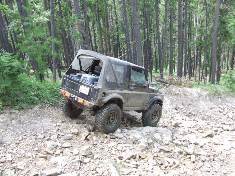 1990 Ford Bronco - Suzuki Samurai navigating a challenging rocky terrain in a forest setting.