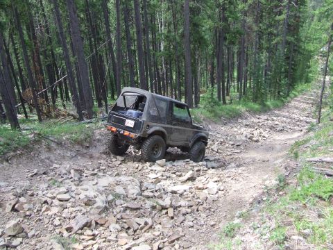 1990 Ford Bronco - A Suzuki Samurai navigates a challenging, rocky path in a dense forest environment.