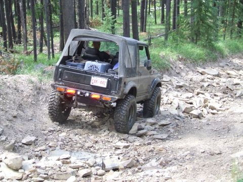 1990 Ford Bronco - A Suzuki Samurai navigates a challenging, rocky off-road trail through a forest.