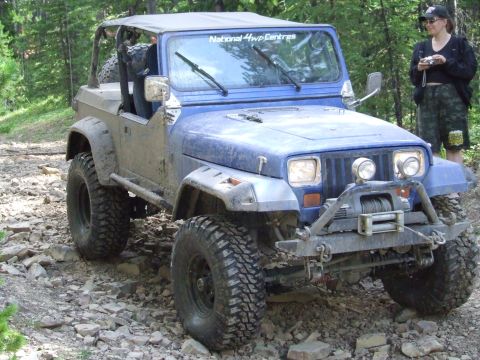 1990 Ford Bronco - A blue Jeep Wrangler navigates a rocky path, its off-road modifications evident.