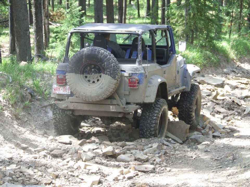 Mud-splattered off-road vehicle with spare tire on back, navigating rocky terrain