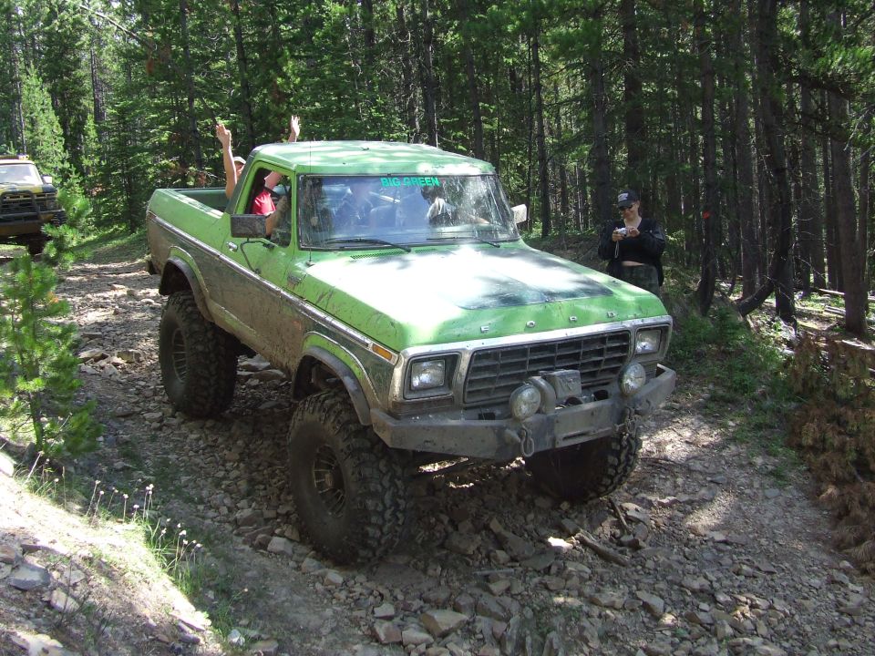 Green lifted pickup truck with people waving, driving on a rocky forest trail