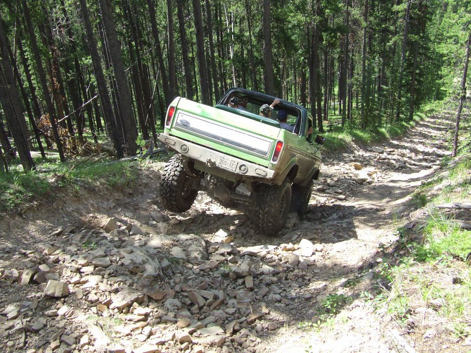 Green Ford Bronco climbing a rocky trail in a forest