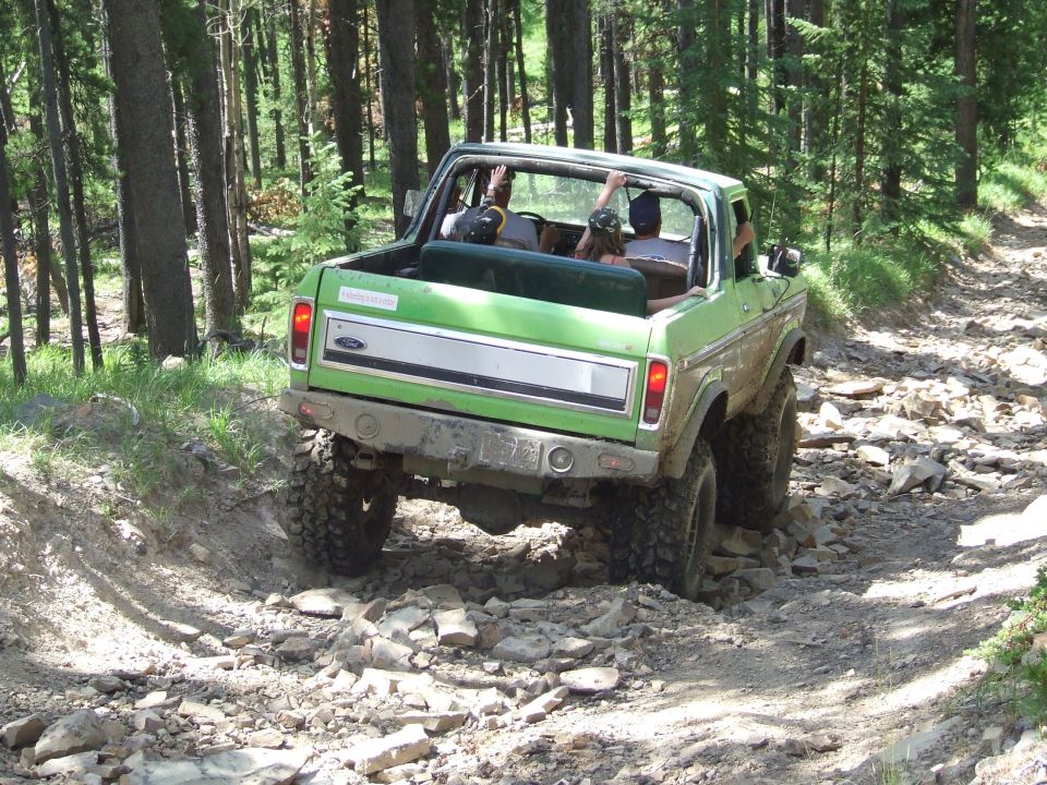 Green 1978 Ford Bronco with people inside driving on a rocky forest trail