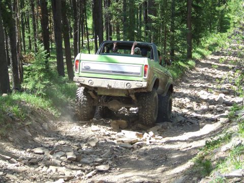 1990 Ford Bronco - This lifted Ford Bronco navigates a challenging, rocky path through a dense forest.