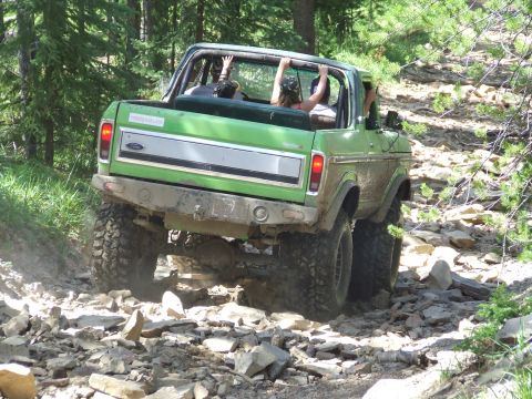 1990 Ford Bronco - A green Ford Bronco navigates a challenging, rocky off-road path with passengers inside.
