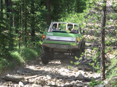 1990 Ford Bronco - Green 1978 Ford Bronco navigates a challenging rocky path through a forest.