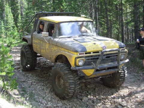 1990 Ford Bronco - A heavily modified Ford pickup truck navigates a rough, rocky path through a wooded area.