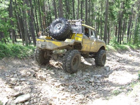 1990 Ford Bronco - This heavily modified off-road truck navigates a challenging rocky trail through a forest.