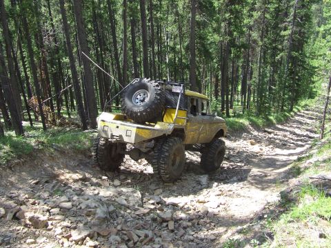 1990 Ford Bronco - A heavily modified yellow pickup truck navigates a rocky, wooded trail.