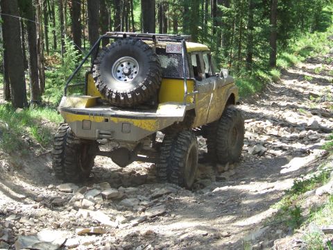 1990 Ford Bronco - Modified yellow truck navigates a rocky trail through a forest.