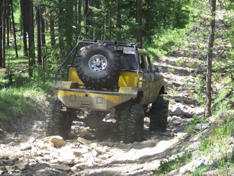 1990 Ford Bronco - Modified pickup truck navigates a challenging rocky trail through a forest.