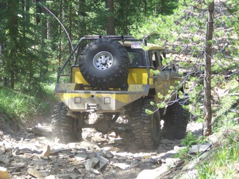 1990 Ford Bronco - This heavily modified off-road vehicle navigates a challenging, rocky path through a wooded area.