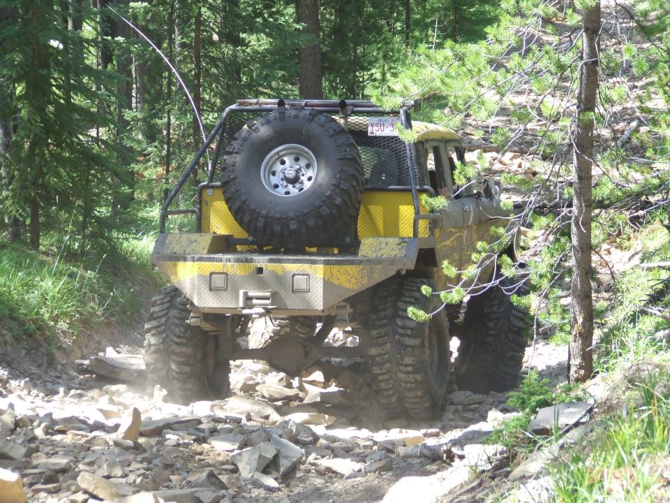 Yellow off-road SUV with a spare tire mounted on the back, driving on a rocky trail