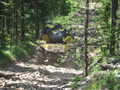 1990 Ford Bronco - An off-road vehicle navigates a challenging rocky path through a dense forest.