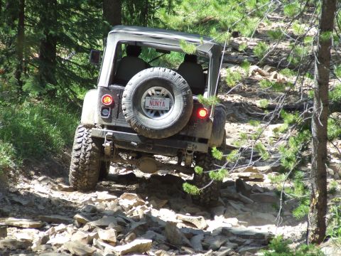 1990 Ford Bronco - A Jeep Wrangler navigates a challenging rocky trail, its rear spare tire prominently displayed.