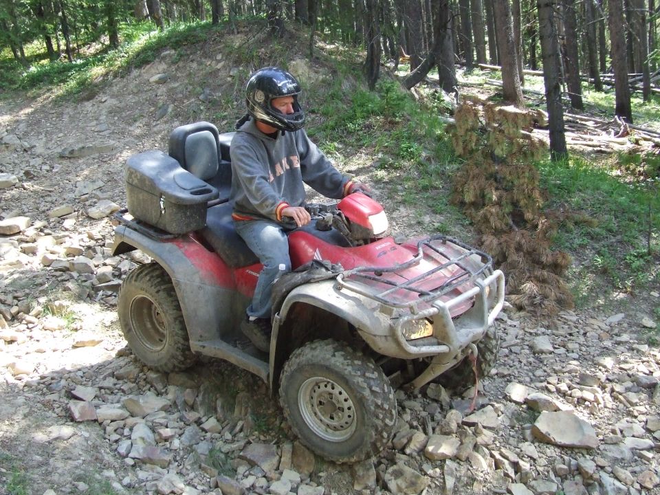 Red ATV with a rider on a rocky forest trail