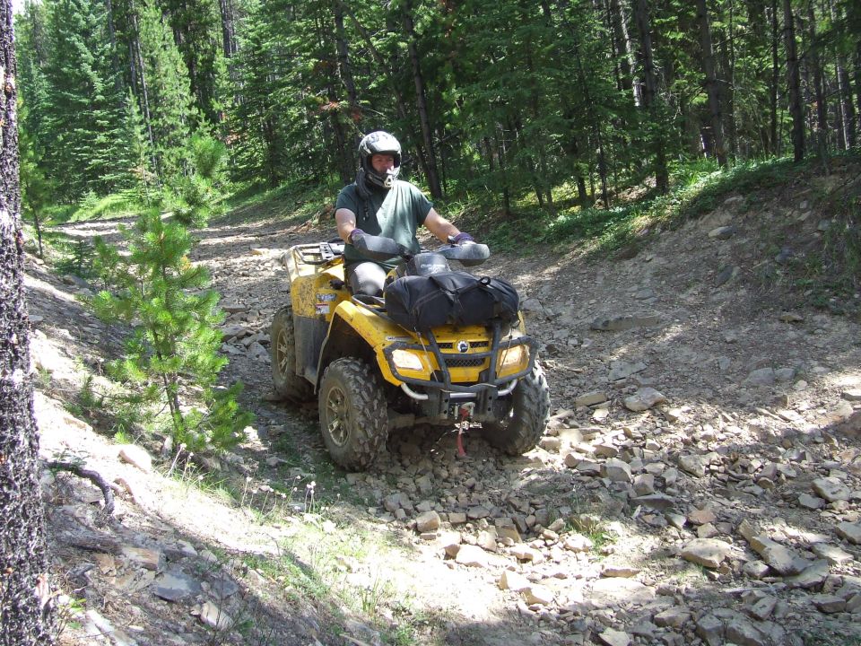 Yellow ATV on a rocky forest trail with a rider wearing a helmet