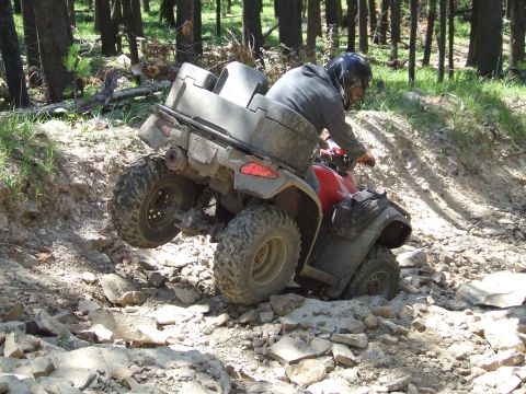 1990 Ford Bronco - An ATV is driven over a rough, rocky terrain in a forest setting.