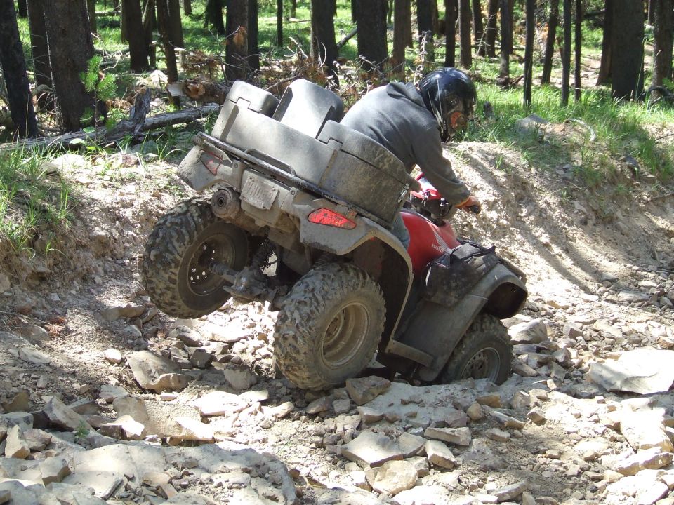 ATV navigating a rocky, wooded trail with the rider wearing a helmet