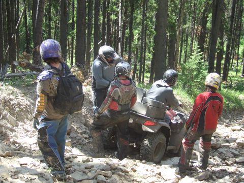 1990 Ford Bronco - A group of riders on ATVs navigate a wooded, rocky terrain.