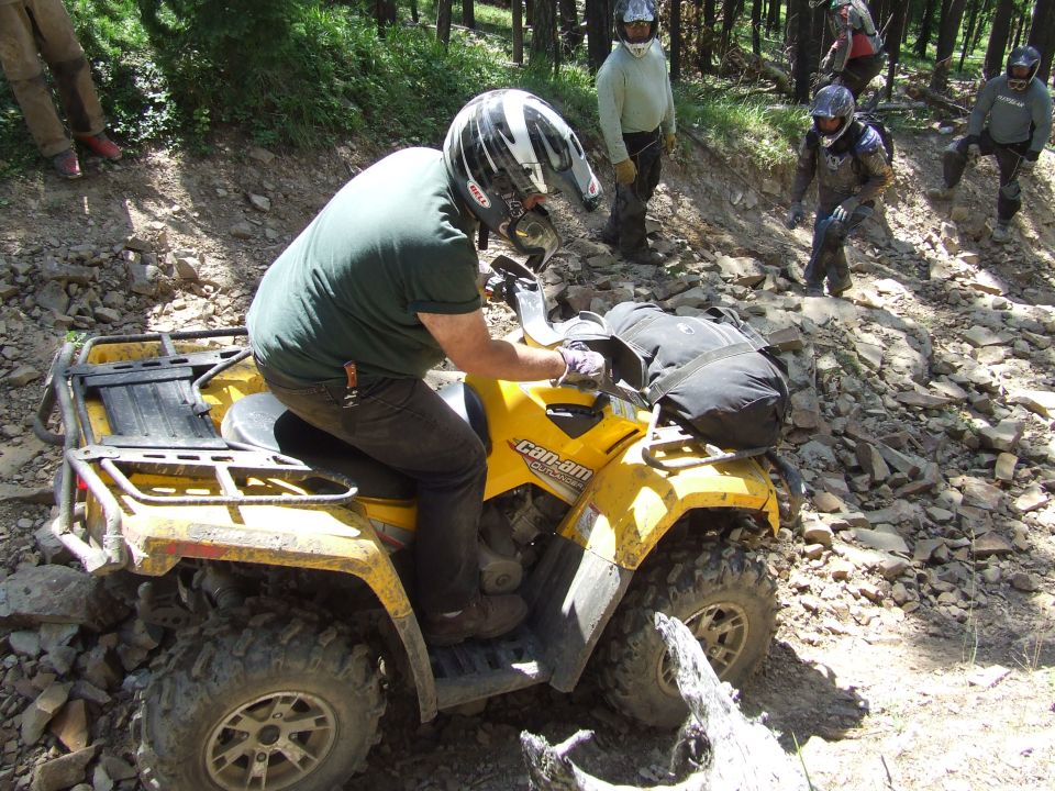 Yellow all-terrain vehicle with a rider on a rocky trail, with other people in the background