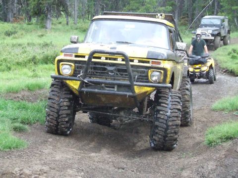 1990 Ford Bronco - A yellow off-road truck leads a convoy of vehicles on a dirt path.